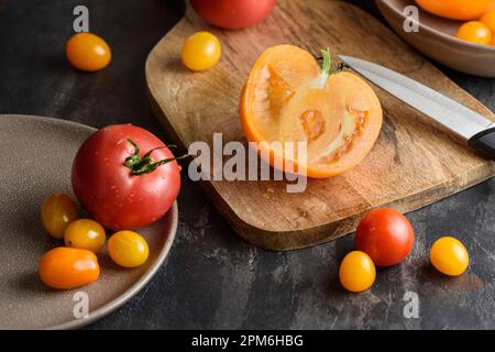 Half a tomato on a cutting board. There are various yellow and red tomatoes nearby. Stock Photo