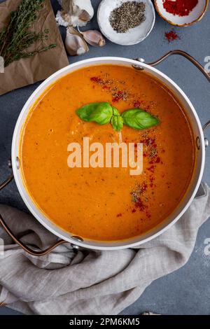 Roasted tomato soup garnished with spices and fresh basil leaves in a pot, black pepper, paprika, garlic and thyme on the side. Stock Photo