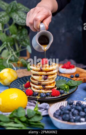 Maple syrup being poured over a stack of pancakes topped with blueberries and raspberries. Stock Photo