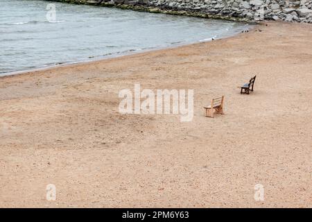 Two wooden benches stand on the beach with sand. Stock Photo