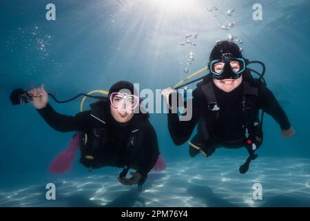 Closeup of two happy scuba divers holding their regulators in their hands underwater with one tongue out and smiling at the camera with the bright sun Stock Photo