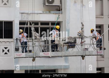 Three workers on the scaffolded elevators in height, working their best to scrap off peel paint, coating new paint on the facade of the building. Stock Photo