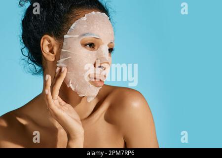 facial hydrating and rejuvenation procedure. African American woman with moisturizing skincare mask on blue background, high quality Stock Photo