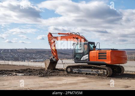 Large orange crawler excavator against backdrop of sky and an overcast dramatic summer sky Stock Photo