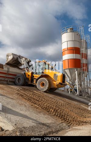The front loader unloads the crushed stone into the making machine concrete. Against the background of the production room. Heavy equipment. Stock Photo