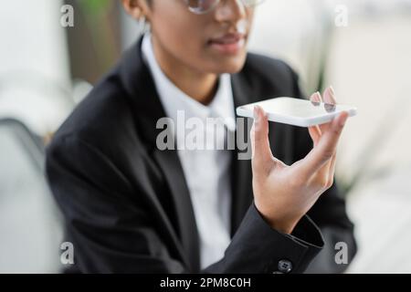 partial view of blurred african american businesswoman sending voice message on smartphone while working in office,stock image Stock Photo