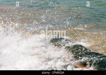 Foamy waves breaking and crashing over seaweed covered rocks. Stock Photo