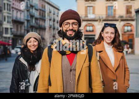 Portrait of group of happy young people smiling together and looking at camera standing outdoors. Front view of three cherful hipsters enjoying a trip at european city. On foreground one bearded man. High quality photo Stock Photo