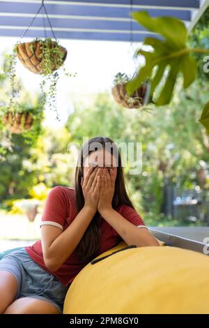 Sad caucasian teenager girl sitting on sofa, covering her face and crying Stock Photo