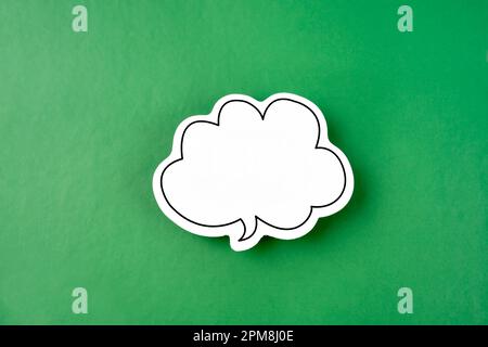 White speech bubble shaped post it note on green background with copy space. Stock Photo
