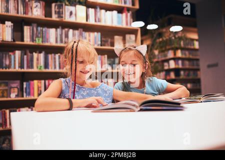 Two elementary schoolgirls doing homework in school library. Students learning from books. Pupils having fun in library. Back to school Stock Photo