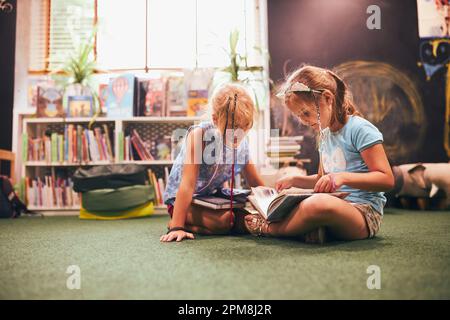 Two primary schoolgirls doing homework in school library. Students learning from books. Pupils having fun in library. Back to school Stock Photo