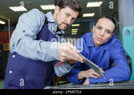 portrait of engineer and apprentice examining component in factory Stock Photo