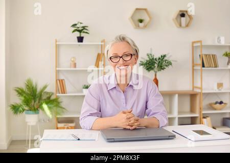 Happy, cheerful, beautiful mature businesswoman sitting at her working desk in the office Stock Photo