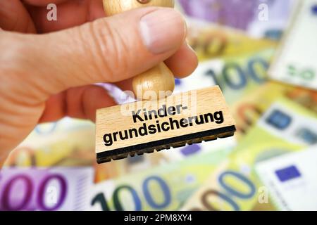 FOTOMONTAGE, Hand hält Stempel mit Schriftzug Kindergrundsicherung über Geldscheinen Stock Photo
