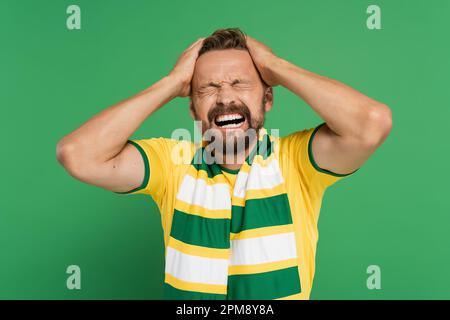 emotional sports fan in striped scarf and yellow t-shirt pulling his hair isolated on green,stock image Stock Photo