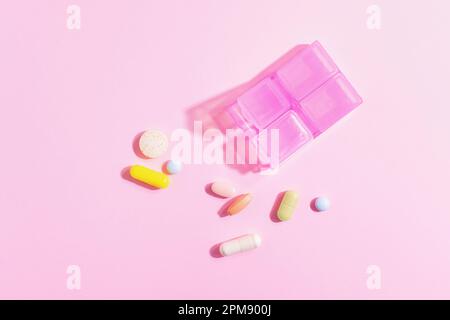 Pink pill organizer with colourful pills and supplements on pink background, top view. Stock Photo