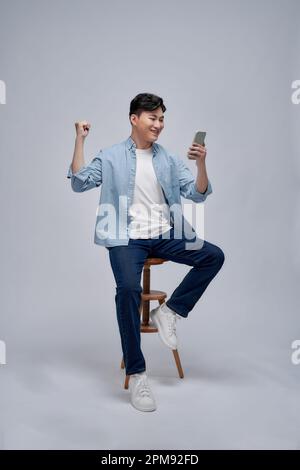 Happy excited Asian man looking at his smartphone and raising his arm up to celebrate success Stock Photo