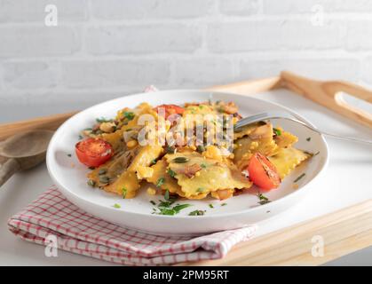 Ravioli with mushroom filling fried in butter with ham and topped with roasted pumpkin seeds and egg yolk crumbs. Stock Photo