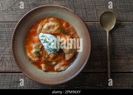 Ukrainian national dish red borscht with dumplings in a ceramic plate on a wooden background. Beetroot soup is a national dish in Ukraine, close up, t Stock Photo