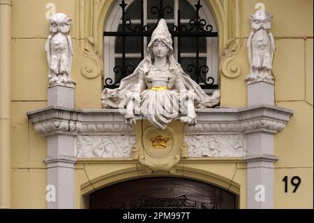 Medieval lady in pointed hat and cloak flanked by two watchful owls as she guards an entrance to an old house in Münsterplatz, Aachen, North-Rhine Westphalia, Germany.  The stucco sculpture is typical of the ‘Historicist’ Gothic and Renaissance revival art and architecture that thrived in the Prussian and German Empire era in the late-1800s and early-1900s. Stock Photo