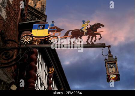 Blue and yellow mail coach guided by postillion blowing a post horn: vintage metal sign promoting Postwagen restaurant beside twisted ‘barley-sugar’ Baroque columns and gilded capitals of the Ratskeller eatery occupying cellars of the medieval Gothic Rathaus or City Hall in Krämerstrasse, Aachen, North-Rhine Westphalia, Germany.  A stained glass lantern hangs from the end of the sign. Stock Photo