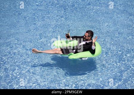 Summer business dreams. Millennial business man in suit floating with  cocktail and laptop in swimming pool. Summer vacation. Funny crazy  businessman Stock Photo - Alamy