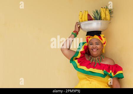 Happy smiling Palenquera fresh fruit street vendor in the Historic District of Cartagena, Colombia. Cheerful Colombian woman in traditional costumes. Stock Photo