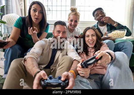 Excited multiethnic teen friends enjoying video games, free time at home, Stock image