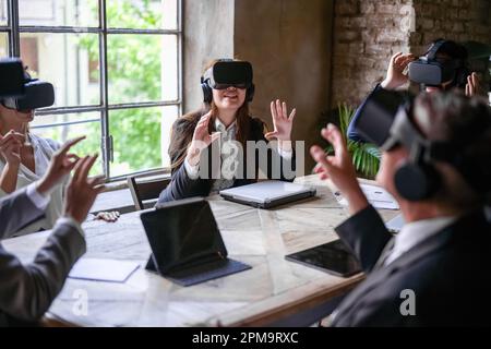 Multiracial business people hi-tech meeting, creative teamwork standing in modern office and using vr headsets, trying new project and gesturing in th Stock Photo