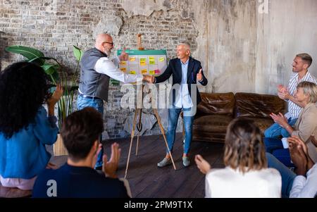 Friendly male leader boss shaking hand of new staff member welcoming male employee on job in corporate department, business colleagues around the offi Stock Photo