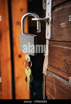 Classic metal padlock hanging at old wooden cottage, keys inside, closeup detail Stock Photo