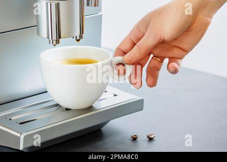 Female hand taking of cup of fresh hot espresso pouring from coffee machine. Professional coffee brewing. Cup of natural espresso. Coffee break. Good Stock Photo