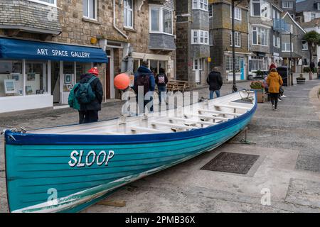 Visitors walking along Wharf Road past a traditional Pilot Gig called Sloop on a rainy chilly miserable day in the historic seaside town of St Ives in Stock Photo