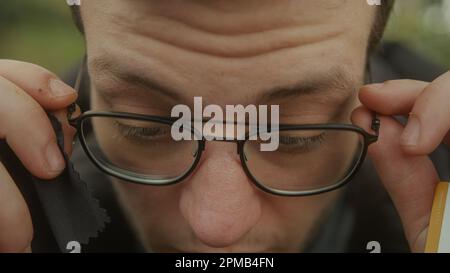 Young man using glasses cleaning cloth to wipe off dust from glasses and wearing them for clear vision - Close-up Shot Stock Photo