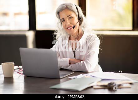 Cheerful Businesswoman Wearing Headset Communicating Online At Laptop In Office Stock Photo