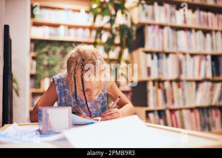 Schoolgirl doing homework. Elementary student learning, drawing pictures, doing puzzles at desk in school library. Primary student in school club. Sma Stock Photo