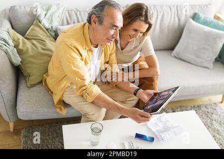 Happy senior couple smiling happily while having video call with family on digital tablet, sitting on sofa at home Stock Photo