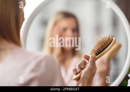 Hairloss. Shocked Blonde Woman Holding Comb Full Of Fallen Hair After Brushing Stock Photo