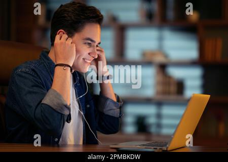 Closeup of young businessman using earphones and laptop, side view Stock Photo