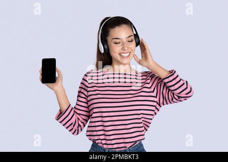 Joyful young woman listening to music in headphones, using smartphone Stock Photo