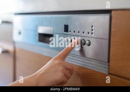 Unrecognizable female turning on dishwasher machine in kitchen Stock Photo