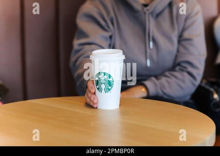 Valencia, Spain : March 18, 2023: Smiling middle aged woman in casual clothes holds a paper cup of hot Starbucks coffee with straw at Starbucks coffee Stock Photo