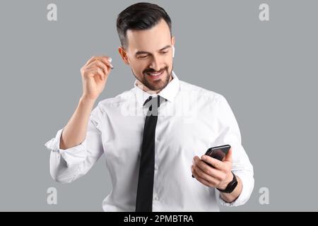 Handsome businessman in earphones using mobile phone on grey background Stock Photo