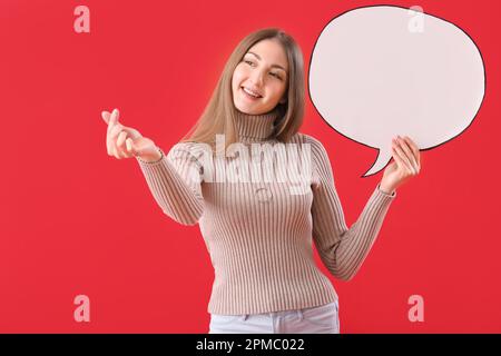 Young woman with blank speech bubble making heart shape on red background Stock Photo