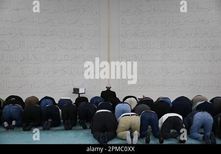 Mainz, Germany. 12th Apr, 2023. Believers have gathered in the prayer room of the Bosnian Mosque of the Islamic Community of Bosniaks (IGDB) in front of the wall relief with Suras 59 (l) and 2 from the Koran for evening prayer. During the fasting month of Ramadan, the Muslim communities in Rhineland-Palatinate also invite non-Muslims to break their fast in the evening (iftar). Credit: Arne Dedert/dpa/Alamy Live News Stock Photo