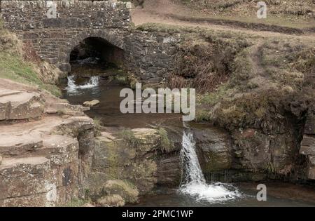 Water flowing under an old bridge over a waterfall into a pool on a dry day Stock Photo