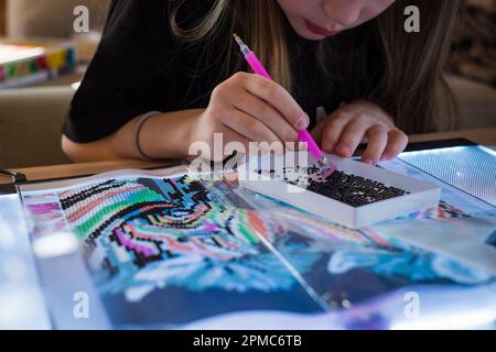 Little girl making diamond painting or pearl mosaic picture. Colorful small pearls stick on image on canvas. Photo series. Stock Photo