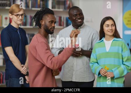 Portrait of young black man playing darts game indoors with diverse group of people and aiming shot Stock Photo