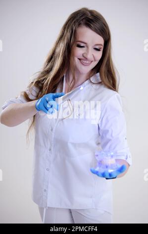 Photopolymer lamp Doctor Fairy with a glowing blue lamp in a white medical suit Dentist treatment of teeth prosthetics put fillings treat gums caries beautiful woman on white background studio ad Stock Photo